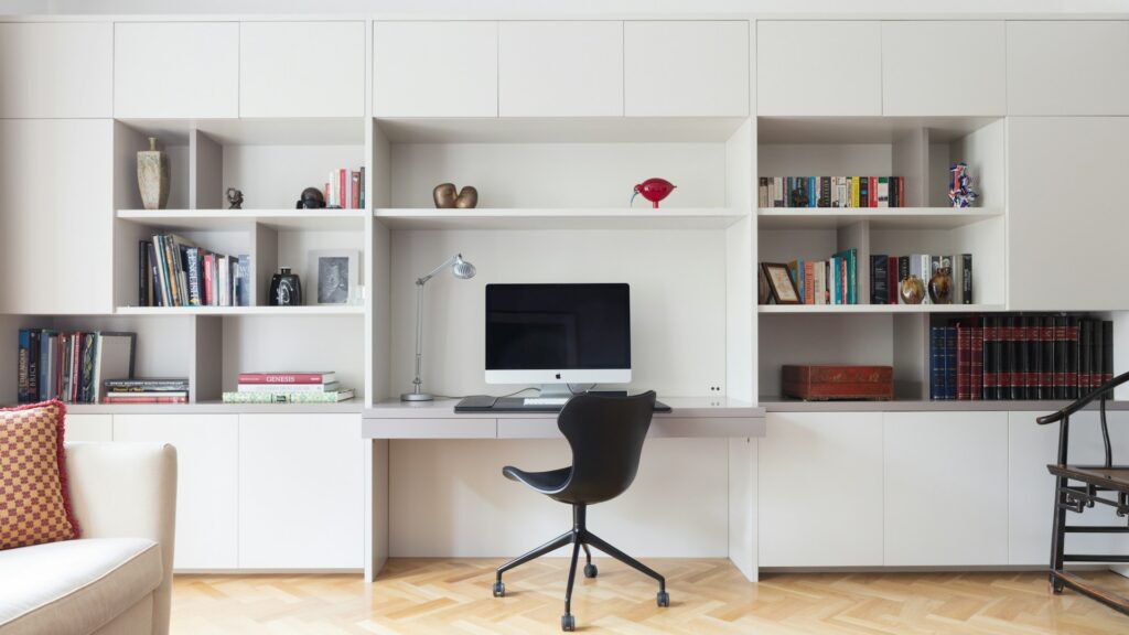 Black rolling office chair beside a white wooden shelf in a modern home office.