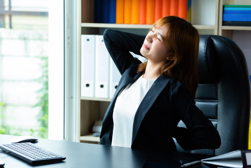 A woman in the office is feeling lower back discomfort while seated, illustrating the importance of ergonomic chairs for back pain.