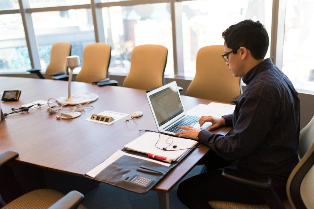 A man using a laptop at a modern conference room table during a meeting showcasing a professional workspace setup with conference room tables.