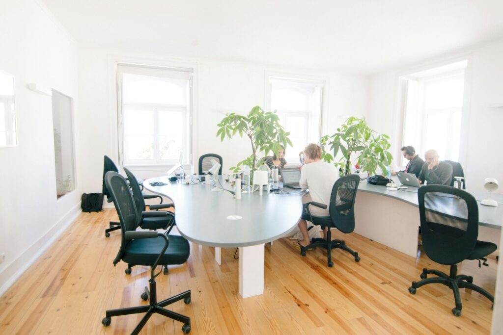 Modern office meeting room with a grey wooden table and black leather rolling chairs arranged around it.